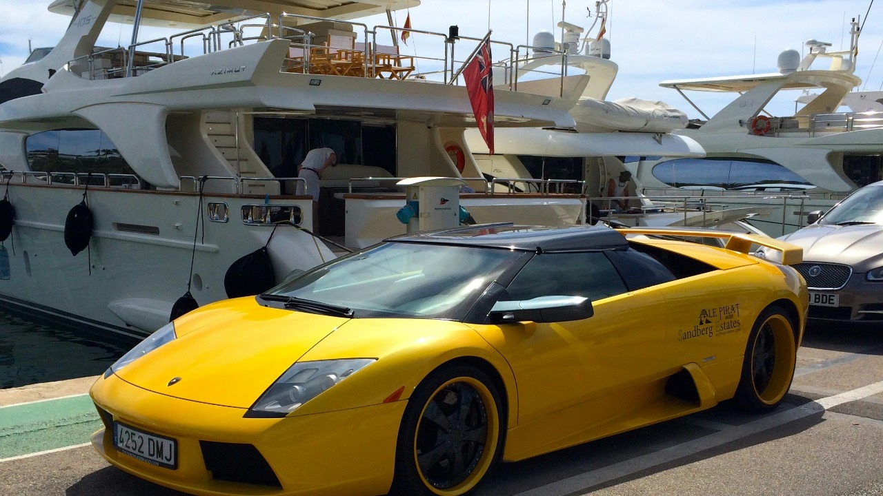 a yellow sports car parked in front of a yacht — Toni Pomar