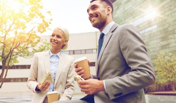 business, partnership, food, drinks and people concept - smiling businessmen with paper cups standing over office building