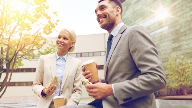 business, partnership, food, drinks and people concept - smiling businessmen with paper cups standing over office building