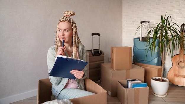 Young woman holding clipboard sitting in box at home