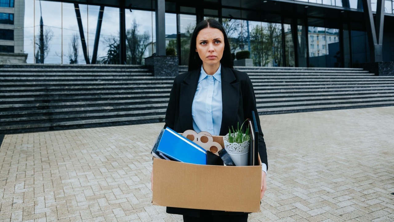 The Struggle of Finding Work After Job Loss An upset woman holds a cardboard box facing the uncertainty of job loss and dismissal