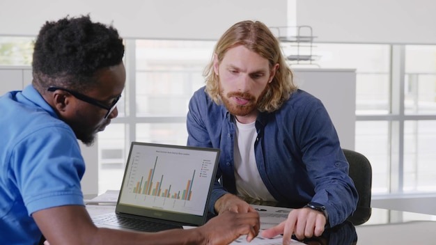 Diverse male startup entrepreneurs discussing company growth looking at graphs and charts