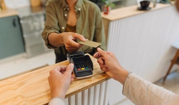 Midsection of female entrepreneur giving credit card to customer at checkout in cafe