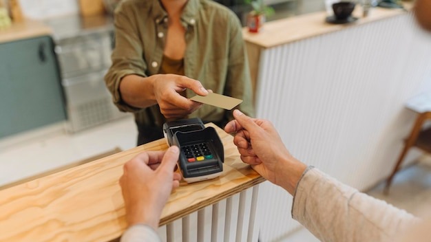 Midsection of female entrepreneur giving credit card to customer at checkout in cafe