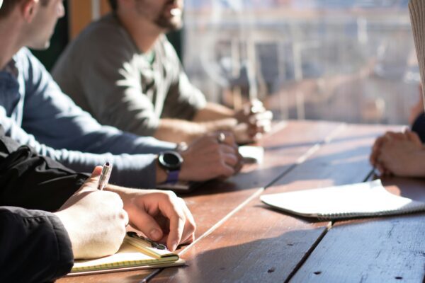 people sitting on chair in front of table while holding pens during daytime