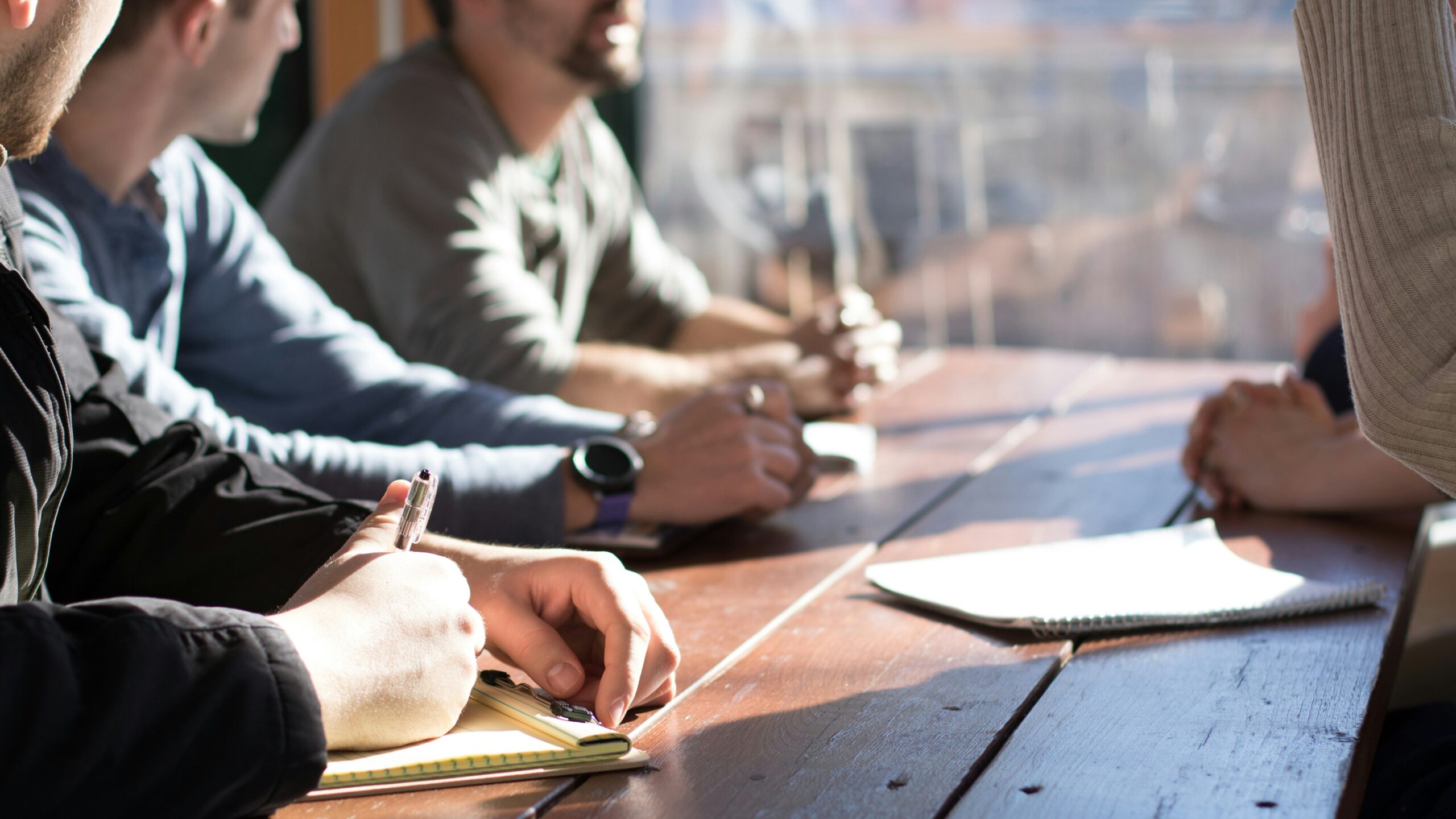 people sitting on chair in front of table while holding pens during daytime
