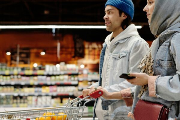 A young couple shopping with a cart in a supermarket aisle, selecting fresh produce.