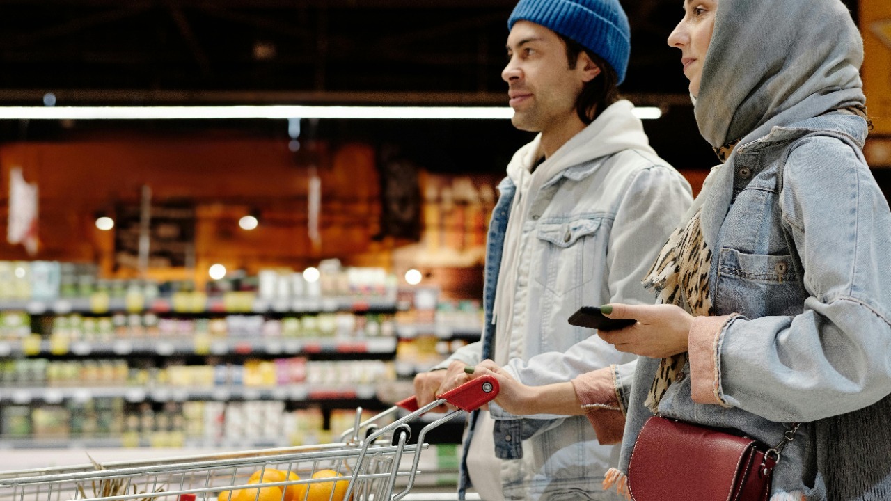 A young couple shopping with a cart in a supermarket aisle, selecting fresh produce.