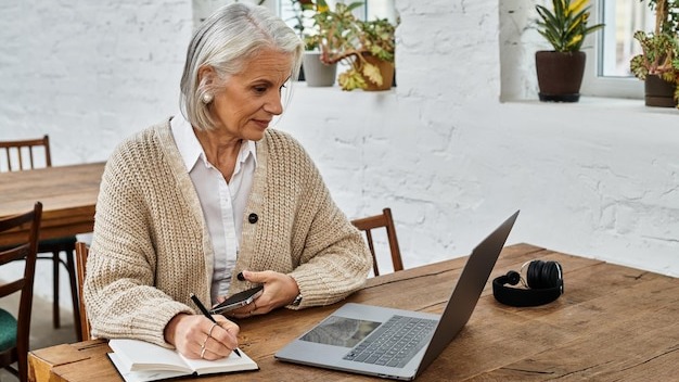 Mature woman with gray hair engaged in online work at a cozy wooden table in a bright space