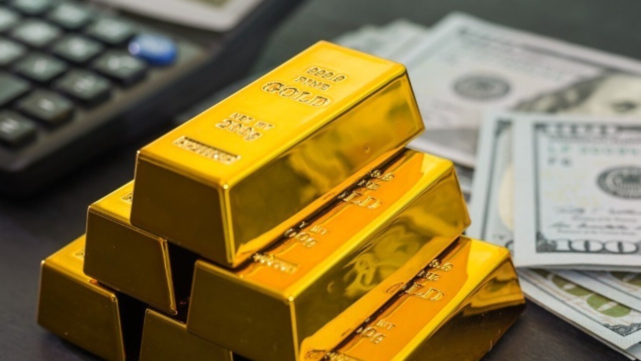 Gold bars with dollars and a calculator on a black wooden table.