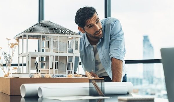 Professional engineer working with house model turning face at laptop tracery