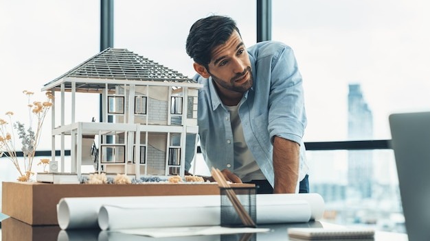 Professional engineer working with house model turning face at laptop tracery