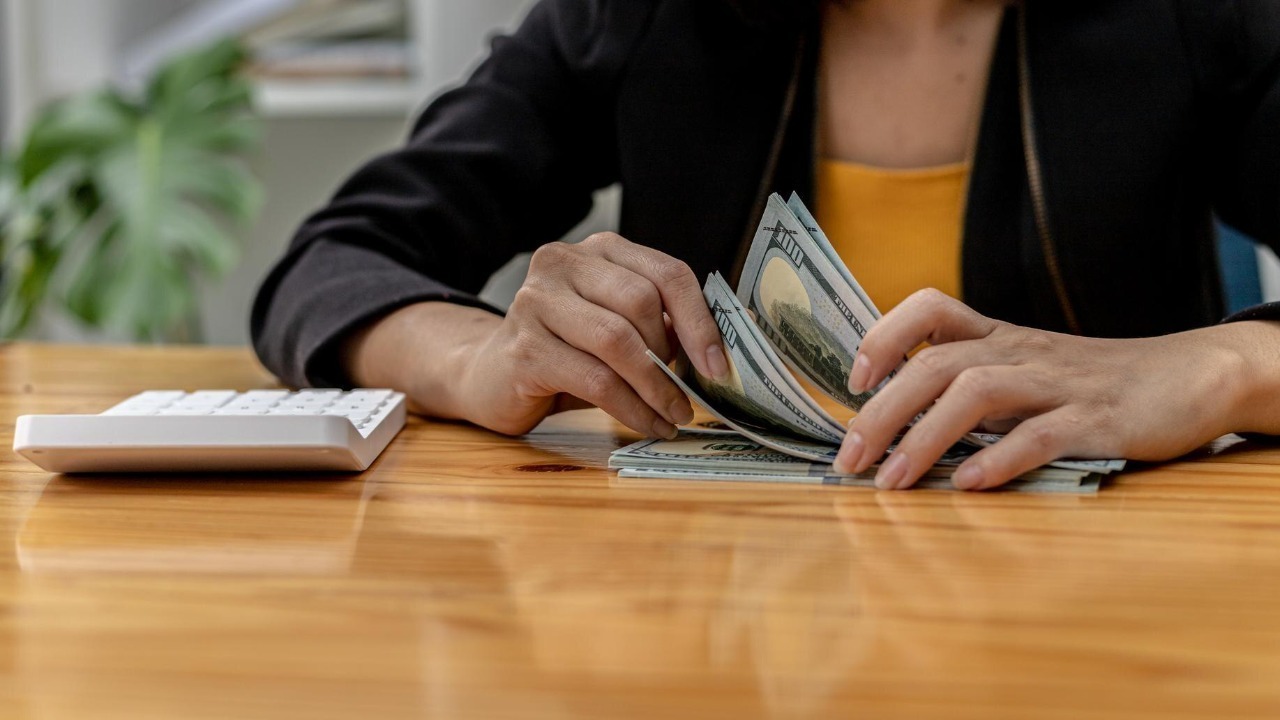 Woman counting dollar bills, she is a cashier serving customers in front of the cashier counter, she counts the money after the service is closed to verify the balance. Conceptual image of money.