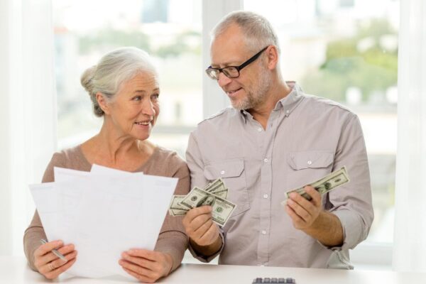 family, savings, age and people concept – smiling senior couple with papers, money and calculator at home