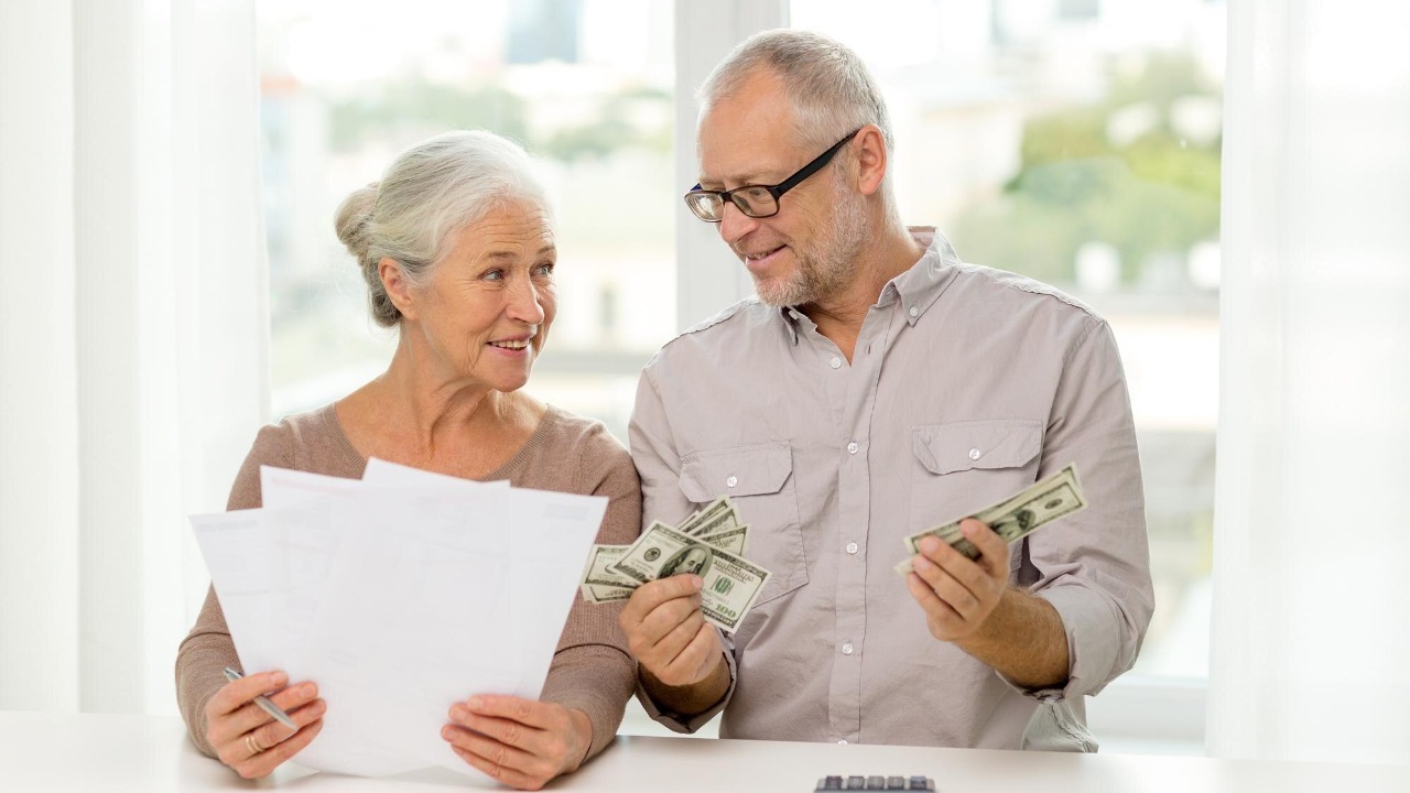 family, savings, age and people concept – smiling senior couple with papers, money and calculator at home