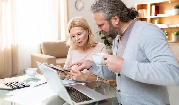 Mature bearded man with cup of tea pointing at document held by his wife while both looking it through