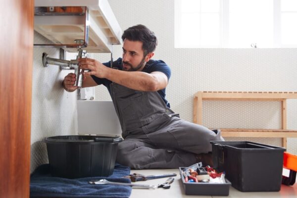 Male Plumber Working To Fix Leaking Sink In Home Bathroom