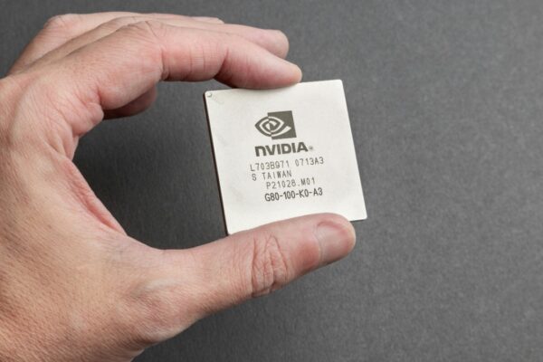 A close-up view of a person holding an Nvidia chip with a gray background.