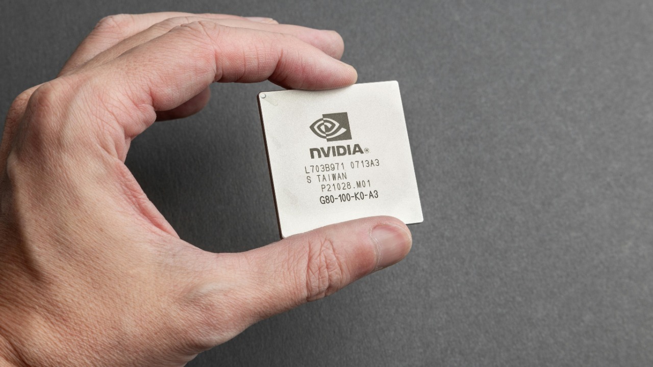 A close-up view of a person holding an Nvidia chip with a gray background.