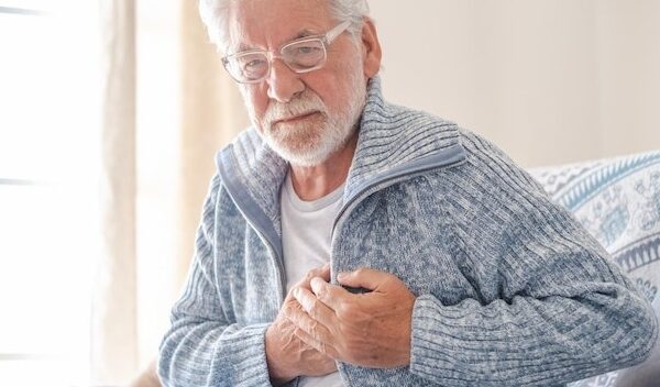 Worried 70s senior man in light blue sweater sitting at home on sofa suffering from bad chest pain elderly heart disease
