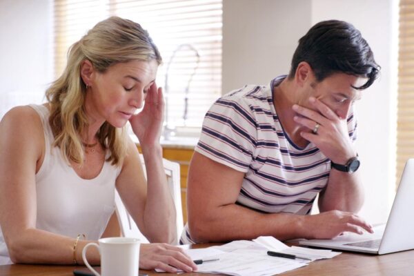 Finance stress and couple with laptop with bills paperwork and online banking issue in debt Home payment due and anxiety from mortgage tax audit or invoice with conversation about savings