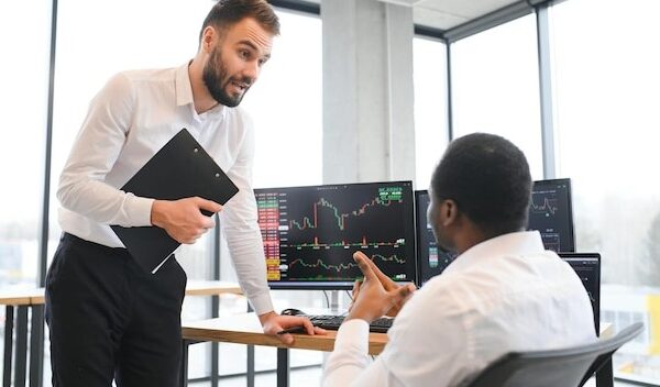 Two men colleagues traders sitting at desk at office monitoring stock market