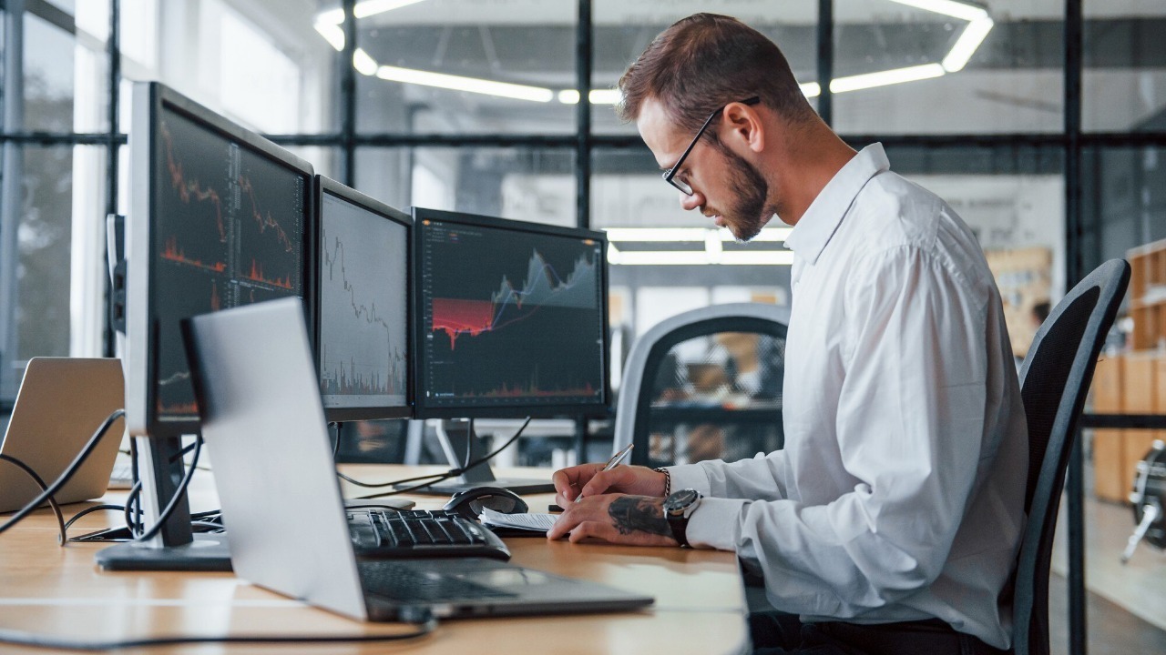 Male stockbroker in formal clothes works in the office with financial market.