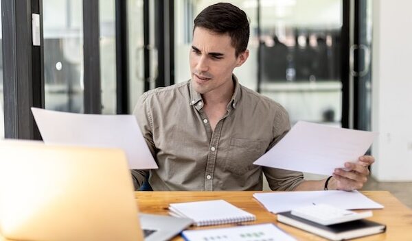 A businessman holding a sales document that the sales department summarizes, he looks displeased when he sees reports of falling sales, he shows signs of stress. Failed sales management concept.