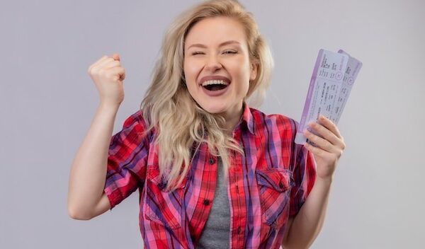 Joyful young female traveler wearing red shirt holding tickets on isolated white wall