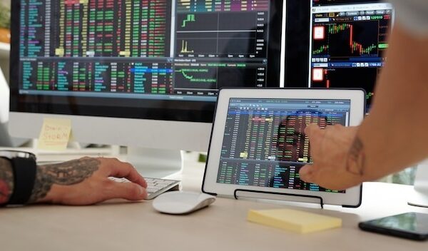 Close-up image of trader checking stock market data on screens of computer and tablet computer
