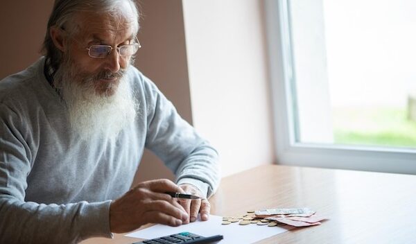 Old bearded senior man with calculator and bills counting euro money and writing notes