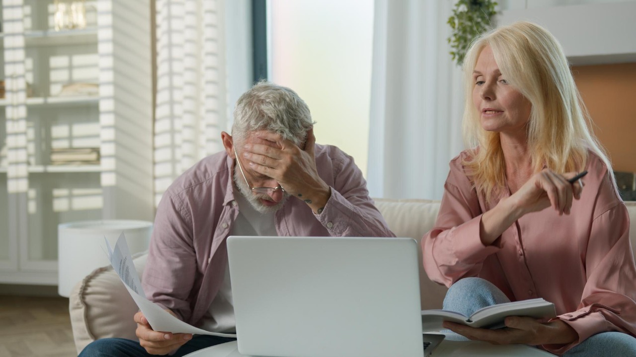Upset retired mature caucasian woman man couple senior elderly male female arguing worrying laptop
