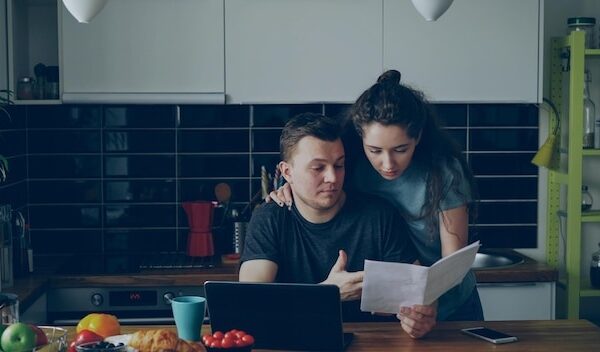 Sad unhappy young man worried about bills payment using laptop in the kithcen at home His girlfrend comes and support him