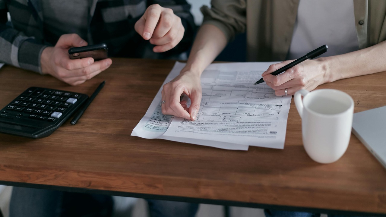 Couple managing finances at home with a calculator, smartphone, and documents.