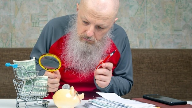 senior man in a red shirt using a magnifying glass to closely inspect his money showing financial