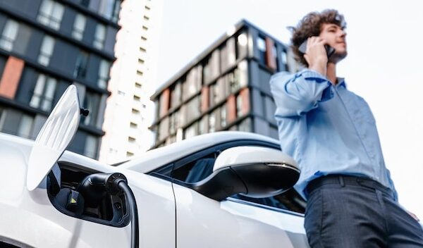 Progressive businessman talking on the phone with recharging electric vehicle