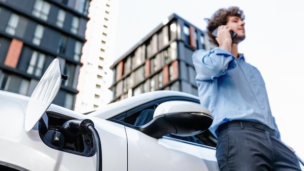 Progressive businessman talking on the phone with recharging electric vehicle