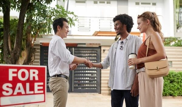 Positive diverse young couple greeting real estate agent in new district