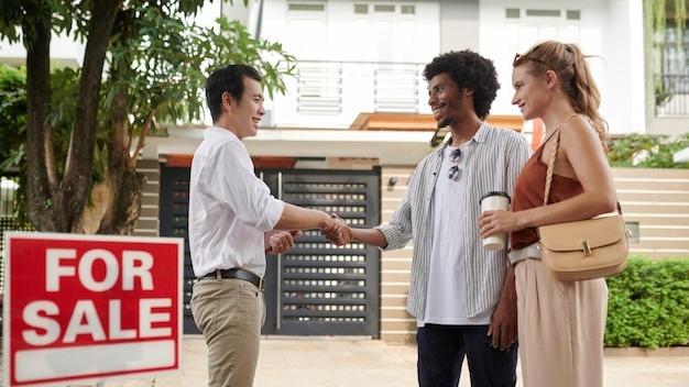 Positive diverse young couple greeting real estate agent in new district