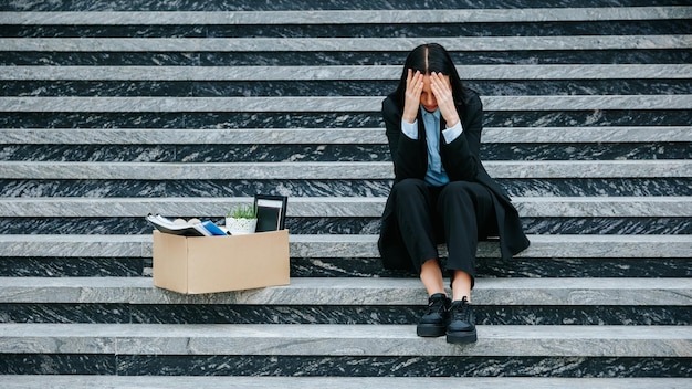 A visual representation of job loss and worklessness as the woman sits on stairs holding a cardboard box Desperate Woman Sitting Alone Outdoors