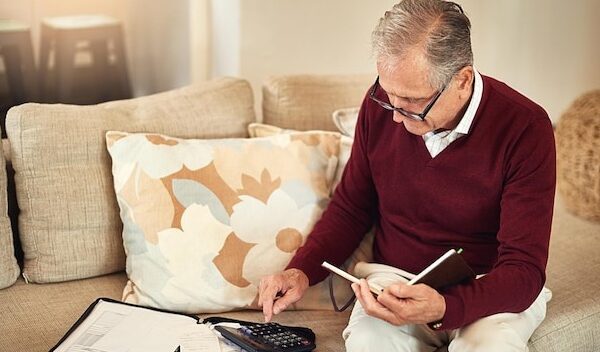 Senior man notebook and calculator on sofa for budget planning and savings account for retirement Elderly person bills and couch in lounge for mortgage personal debt and loan repayment ay home