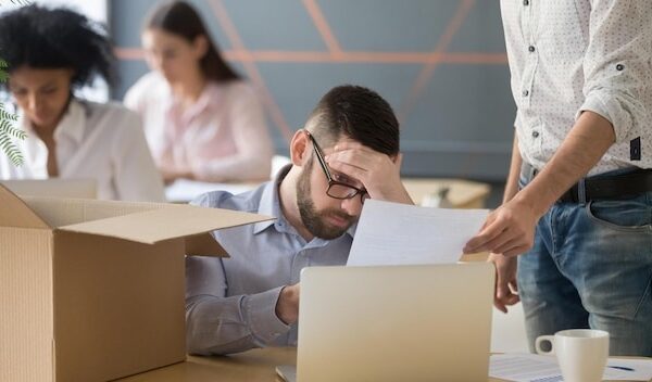 Frustrated upset male employee receiving unfair dismissal notice getting fired from job at workplace depressed stressed office worker about to pack box on last working day being laid off concept