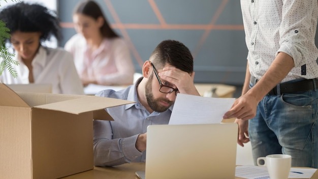 Frustrated upset male employee receiving unfair dismissal notice getting fired from job at workplace depressed stressed office worker about to pack box on last working day being laid off concept