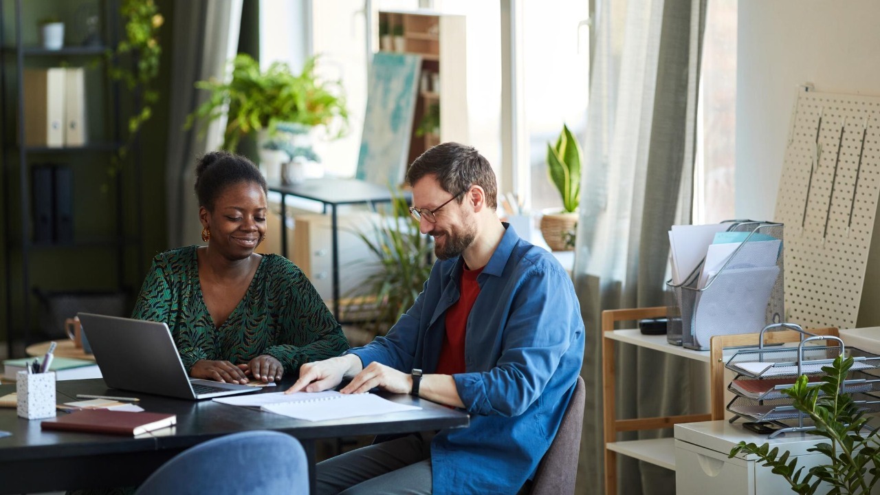 Happy young businessman pointing at his notes in copybook during discussion of data with african ame
