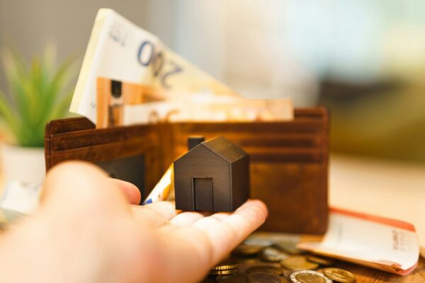 A person holding a small house and some money