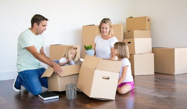 Mom, dad and little daughters unpacking things in new apartment, sitting on floor and taking objects from open boxes