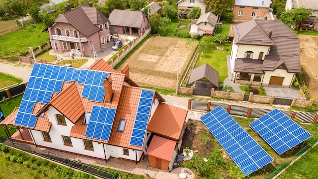 Aerial top view of new modern residential house cottage with blue shiny solar photo voltaic panels system on roof. Renewable ecological green energy production concept.