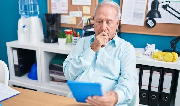 Middle age greyhaired man business worker using touchpad with serious expression at office