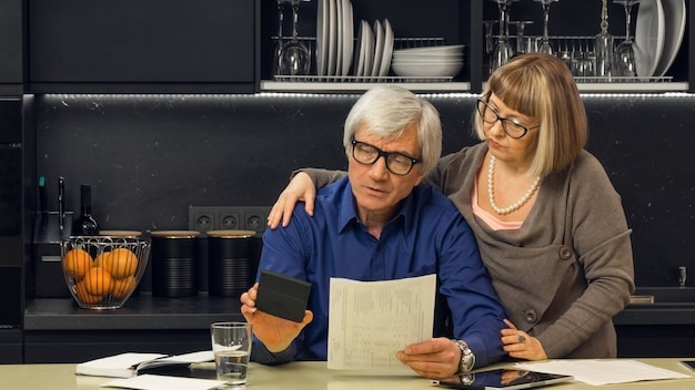 Senior couple calculate their bills on kitchen