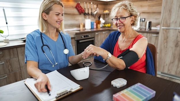 Nurse checks the blood pressure of a cheerful elderly woman in a cozy kitchen
